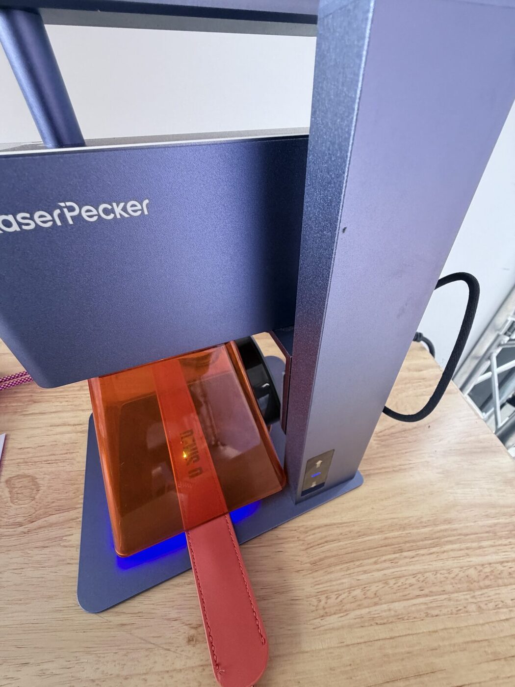 Tabletop laser engraver personalizing a red leather strap at the patch bar's engraving desk