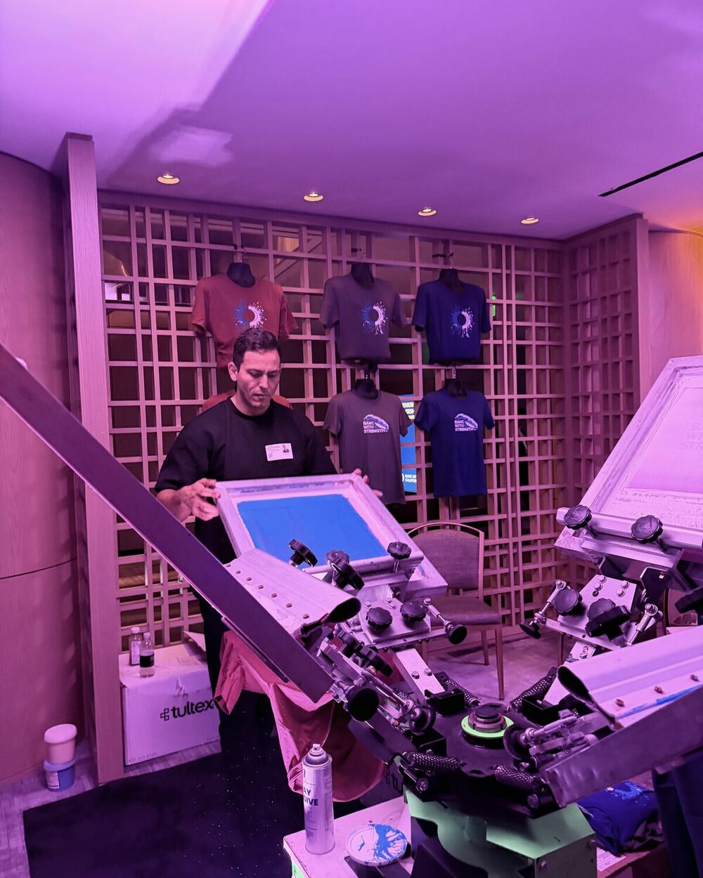 Crew member working a station in front of a wall of finished display shirts