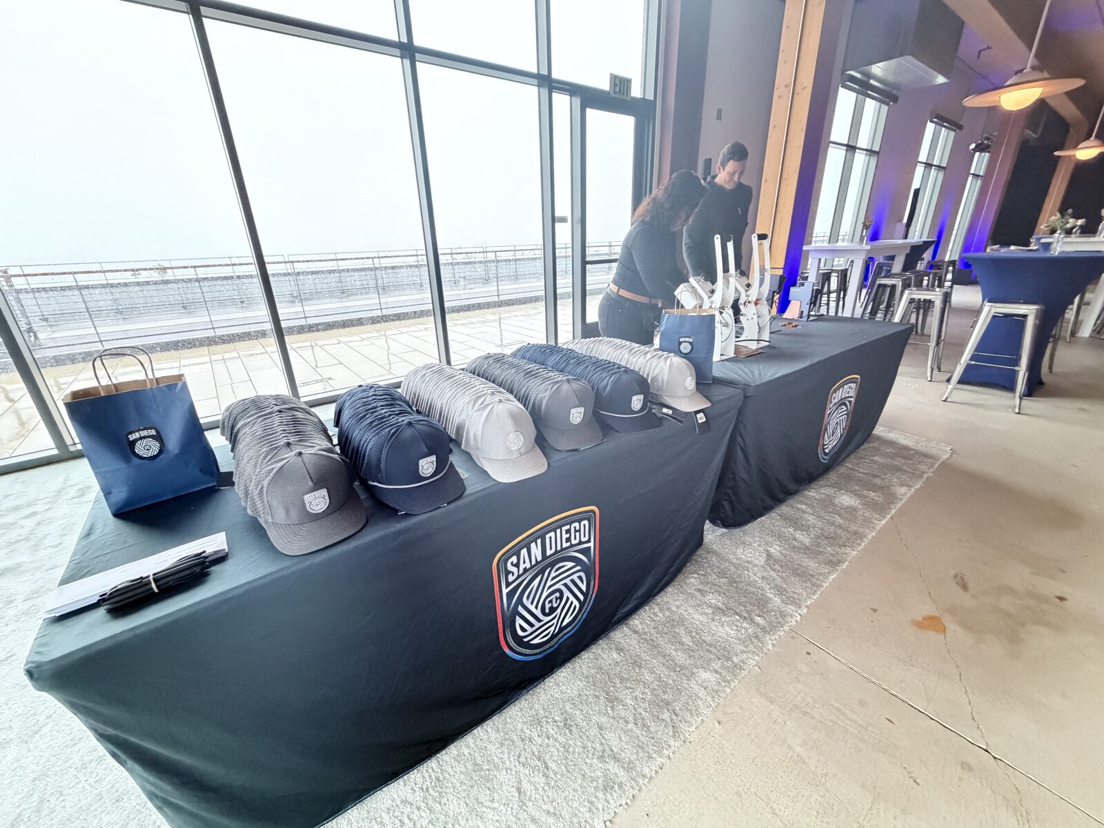 Mobile patch bar table stacked with trucker hats and compact patch presses at a waterfront event space